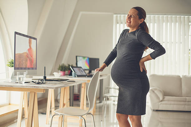 Pregnant mid adult woman standing by the desk in the office, having back pain at the end of pregnancy.